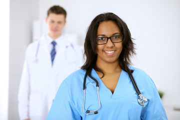 Fototapeta premium Female african american medical doctor with colleagues in background at hospital. Medicine and health care concept