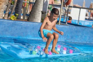 Naklejka premium Smiling Caucasian boy having fun in swimming pool at resort. He is standing on inflatable mattress and ready to jump from it.
