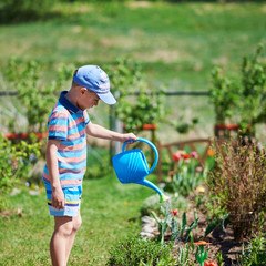 Cute European boy is watering flowers in the countryside croft. He is enjoying his job. © Artem