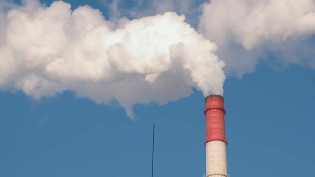 One red and white pipe of thermal power station with smoke in sky background.