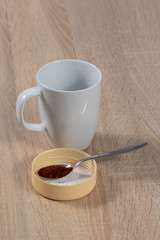 Cup of coffee behind a silver spoon with instant coffee on a wooden table