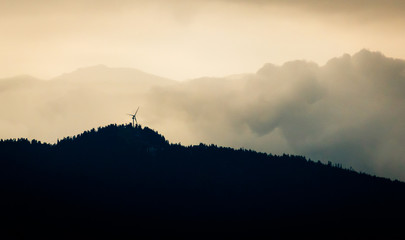 Windmill on Mountain Peak Silhouetted Against Bright Cloudy Sky
