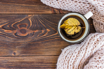 Mug of tea and autumn maple leaves on wooden background.