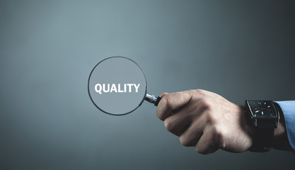 Male hand holding magnifier with word Quality. Searching quality