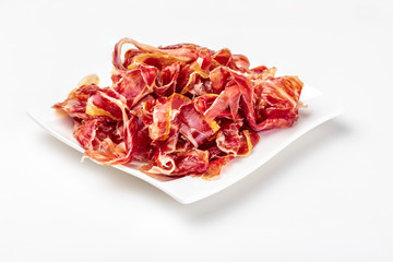 Appetizing slices Iberian ham on a plate. Isolated on white background. Raw meat that becomes an article of haute cuisine and gastronomic luxury, through a process of raw salting and natural curing.