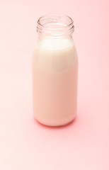 Milk in glass bottle. On delicate light pink background.