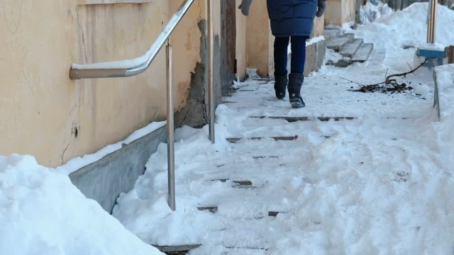 Slippery stairs. Unrecognizable woman in a blue down jacket walking up a snowy staircase in street.