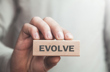Businessman showing Evolve word in wooden block. Business concept