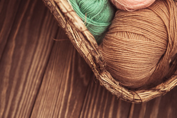 top view of brown and green woolen tangles of threads in wicker basket on wooden knitting background