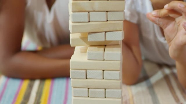 Close up shot of two interested black girls of primary school age playing game together and removing wooden building blocks from toy tower