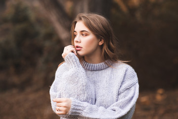 Stylish teen girl wearing knitted cozy sweater posing outdoors. Autumn season. 20s.