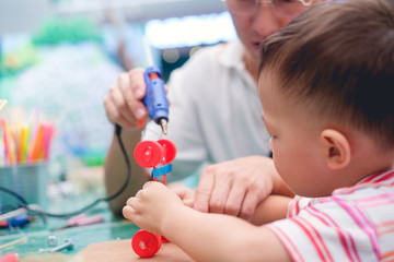 Asian Father teaching kid make car toy with recycled materials, Little 2 years old toddler boy child make D.I.Y reuse toy with dad in workshop, Reduce, Reuse & Recycle concept, Shallow DOF, Soft focus