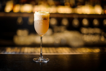 White achoholic drink in the cocktail glass decorated with brown sugar and zest