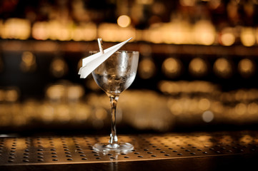 Empty cocktail glass decorated with a paper plane on the bar counter