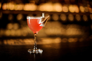Glass of a delicious red cocktail decorated with a paper plane standing on the bar counter