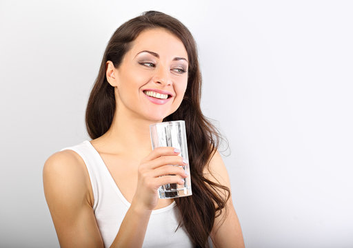Positive happy woman with healthy skin and long curly hair drinking pure water on white background with toothy smile