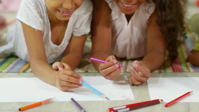Tracking shot of group of black children lying on floor and drawing pictures together with colored pencils, close up