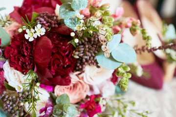 Wedding decor. Classy bouquet of roses, dark pink shoes and golden accessories for a bride lie on the table