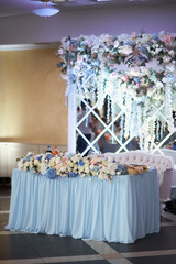 Head table at the reception stands before the glass wall with flowers