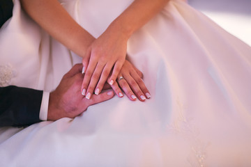 Bride and groom hold their hands together on her knees