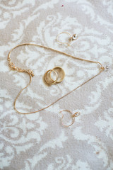 Wedding accessories. Golden necklace, earrings and wedding rings lie on the bed
