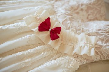 Bride's garter with red bow lies on rich wedding dress