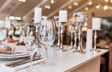 Wedding table serivce. Candles on silver vases and glasses with water stand among white flowers on wedding dinner table
