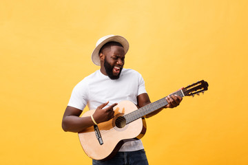 Muscular black man playing guitar, wearing jeans and white tank-top. Isolate over yellow background.