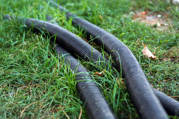 PVC corrugated pipe for communication, black pipe lies on the green grass close-up.