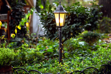 a decorative iron lantern tied with a garland illuminates a green garden with plants.