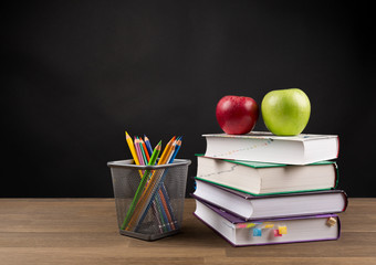Back to School Concept, Stacked books, Coloring Pencils and red and green apple on wooden table isolated on black blackboard background, copy space