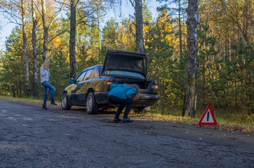Young woman talking on a cell phone by trying to get help from someone to fix problem of her broken car,and her friend waiting support