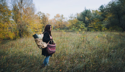A girl in a coat with a backpack in an autumn forest stands in profile. Autumn concept.