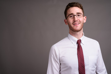 Young handsome businessman wearing eyeglasses against gray backg