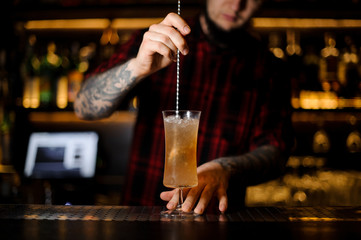 Bartender stirring with a spoon a yellow achoholic drink in a cocktail glass with ice