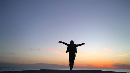 The girl is standing against the sunset and enjoying. girl stands on railing and raises her hands...