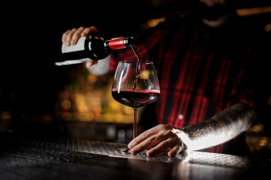 Professional bartender pourring a wine from a bottle to a glass