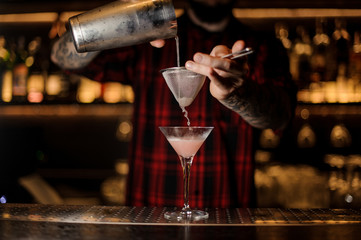 Fototapeta na wymiar Professional bartender pourring a Cosmopolitan from a shaker to a glass