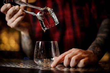 Fototapeta na wymiar Bartender hand putting a big ice cube into a whiskey dof using tongs