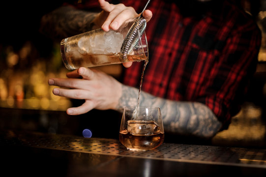 Tattooed barman pouring fresh drink into a whiskey dof glass