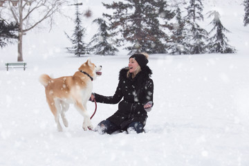 Woman and her dog akita play in park on snowy day. Winter concept
