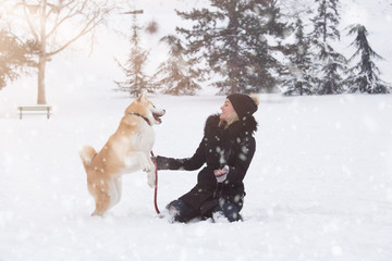 Young woman and her dog akita play in park on snowy day.