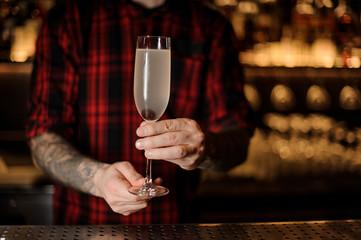 Bartender with tattoos holding a French 75 cocktail