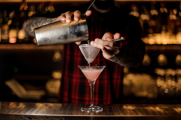 Fototapeta na wymiar Barman pouring Cosmopolitan cocktail into a glass