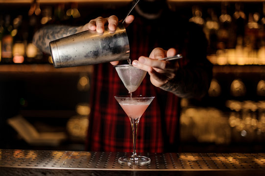 Barman pouring Cosmopolitan cocktail into a glass
