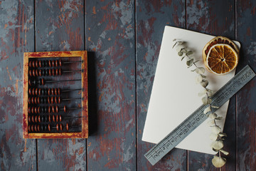 vintage abacus with notebook, pen and dried orange slices on rustic wooden table, hugge concept, top view