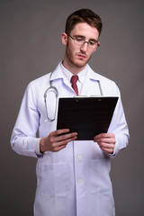 Young handsome man doctor wearing eyeglasses against gray backgr