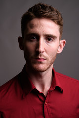 Young handsome businessman wearing red shirt against gray backgr