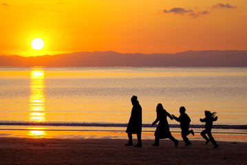 シルエットの四人家族が歩く夕日が沈む美しい海岸