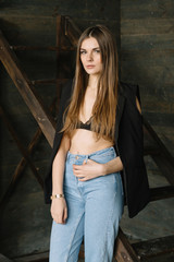 Portrait of a young, attractive student girl. She is serious and standing in the sun against a wooden background near ladder. Fashion pose